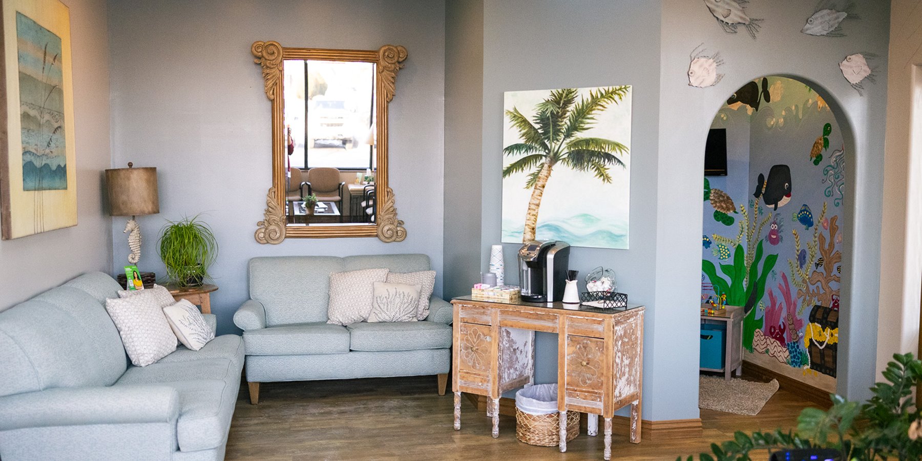 Dental office waiting area with blue couches and palm tree murals